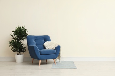 Photo of Stylish room interior with comfortable armchair and plant near beige wall. Space for text