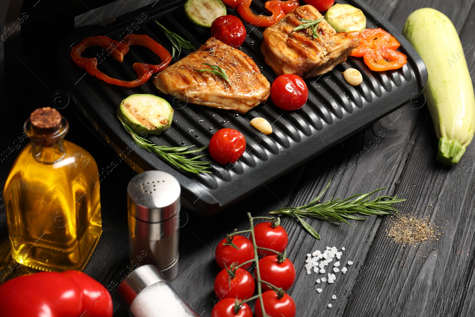 Photo of Electric grill with different products on black wooden table