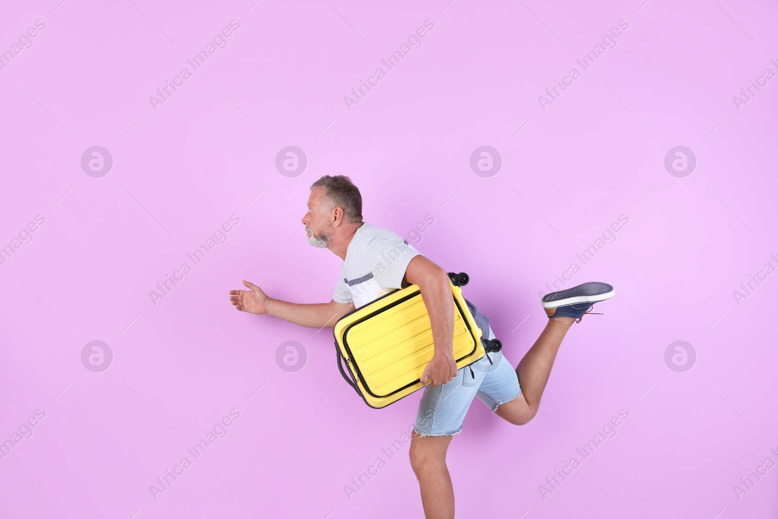 Photo of Senior man with suitcase running on color background. Vacation travel