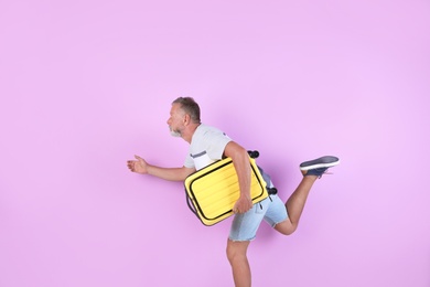 Photo of Senior man with suitcase running on color background. Vacation travel