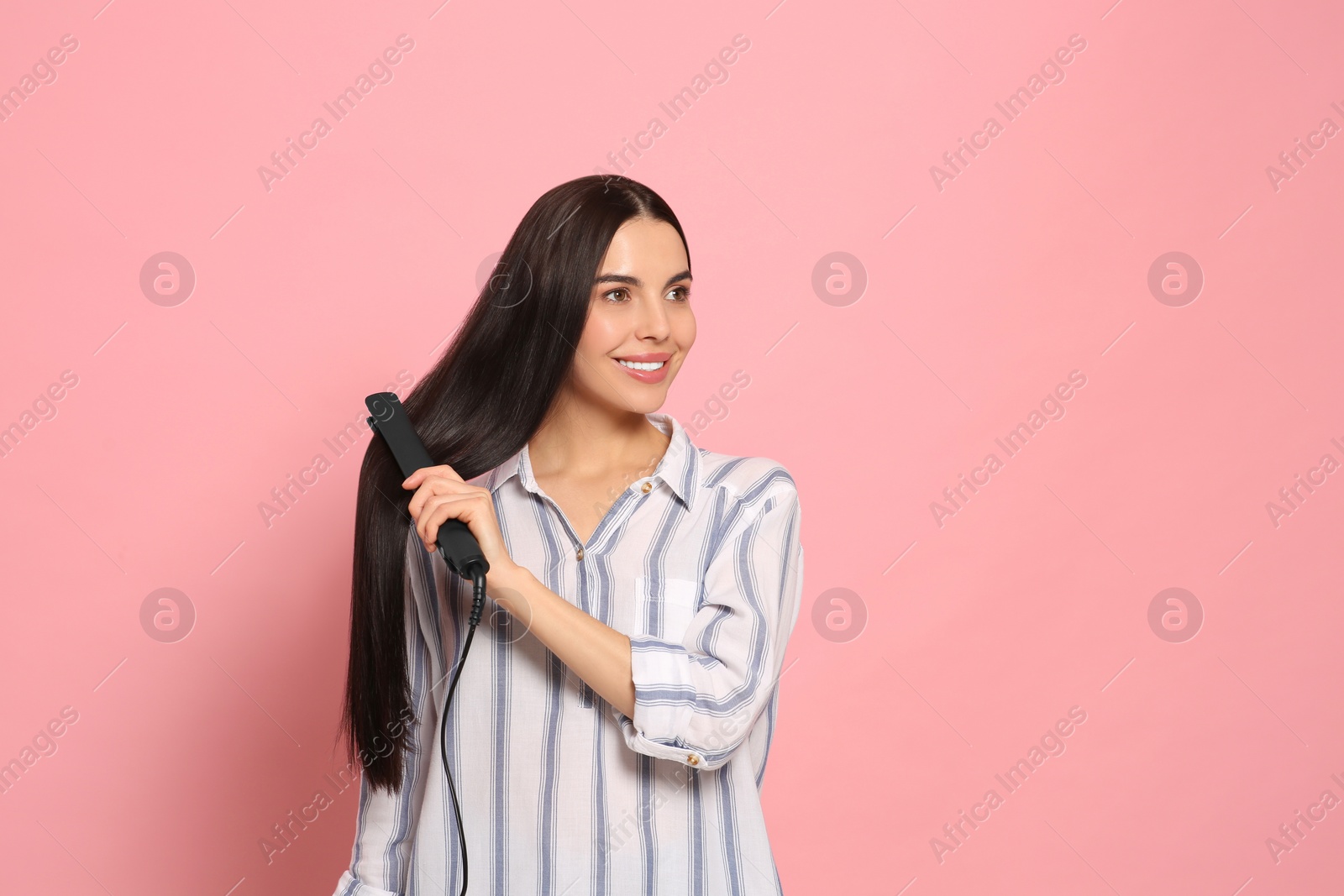 Photo of Beautiful happy woman using hair iron on pink background. Space for text