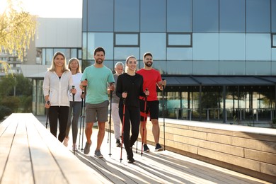 Group of people practicing Nordic walking with poles outdoors on sunny day