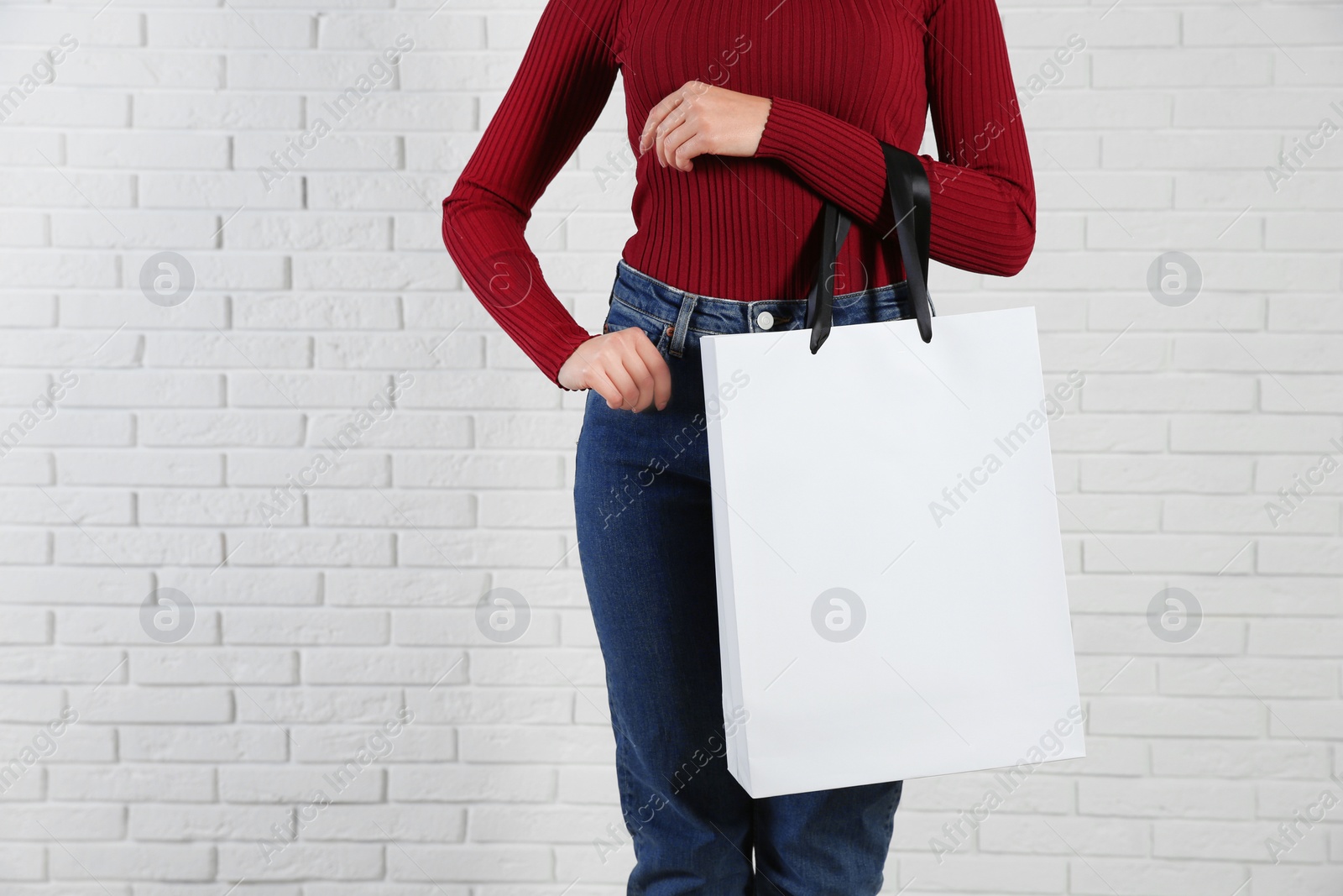 Photo of Woman holding paper shopping bag near brick wall. Mock up for design