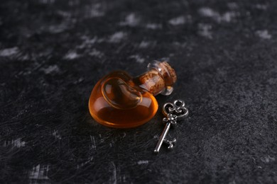 Photo of Heart shaped bottle of love potion with small key on black textured table
