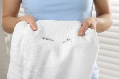 Woman holding terry towel with mascara spot indoors, closeup. Makeup removal