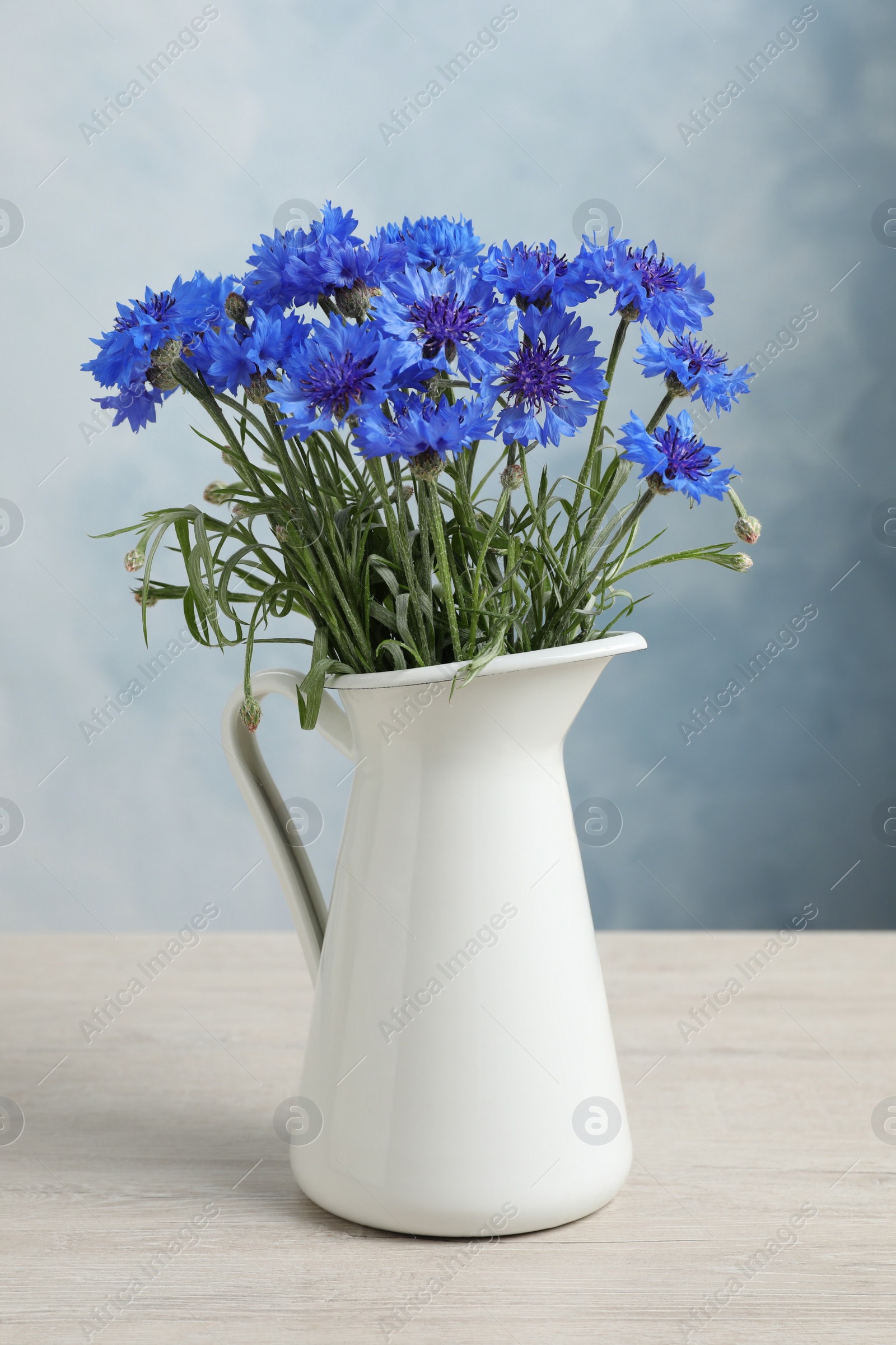 Photo of Bouquet of beautiful cornflowers in vase on white wooden table
