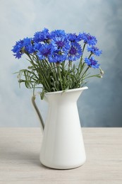 Photo of Bouquet of beautiful cornflowers in vase on white wooden table