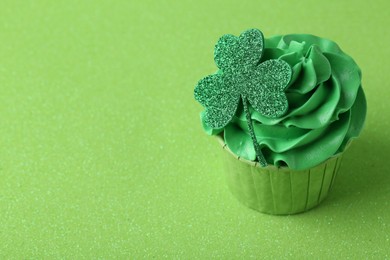 St. Patrick's day party. Tasty cupcake with clover leaf topper and cream on green background. Space for text