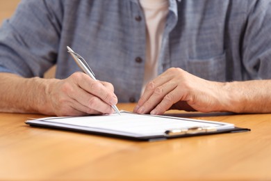 Photo of Senior man signing Last Will and Testament at wooden table, closeup