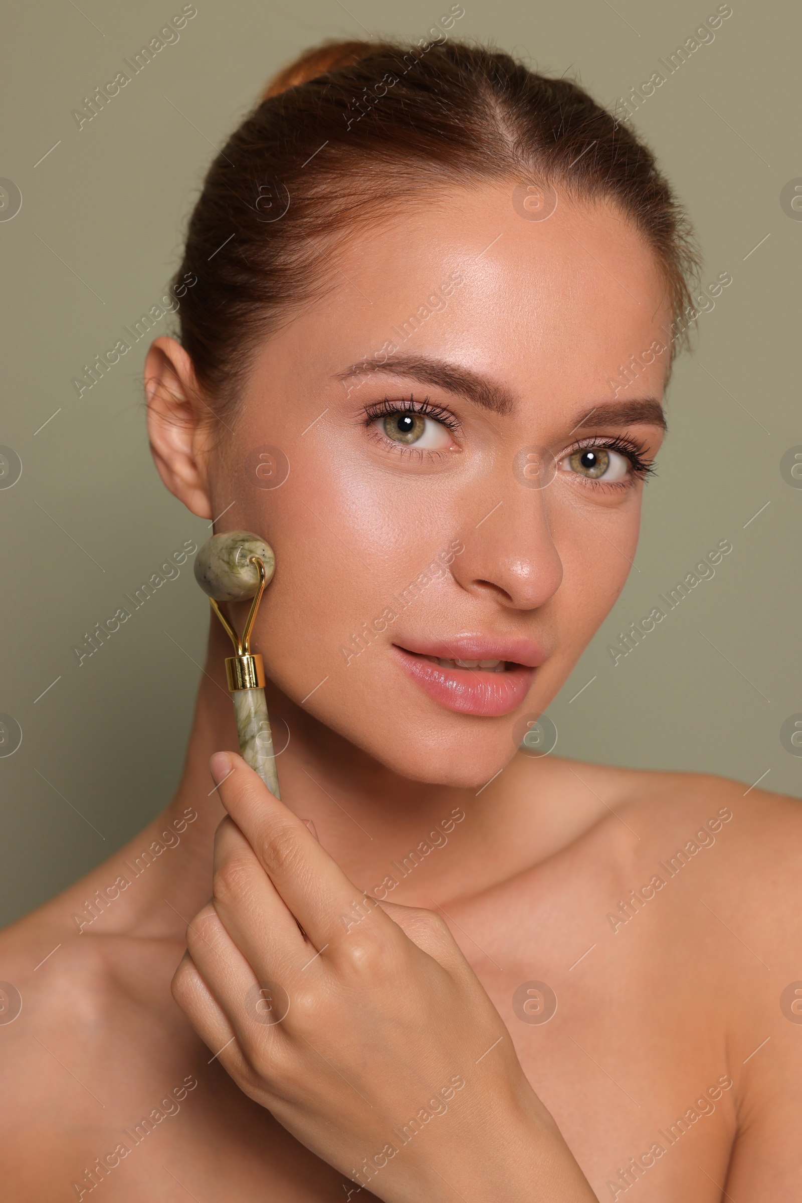 Photo of Young woman massaging her face with jade roller on green background