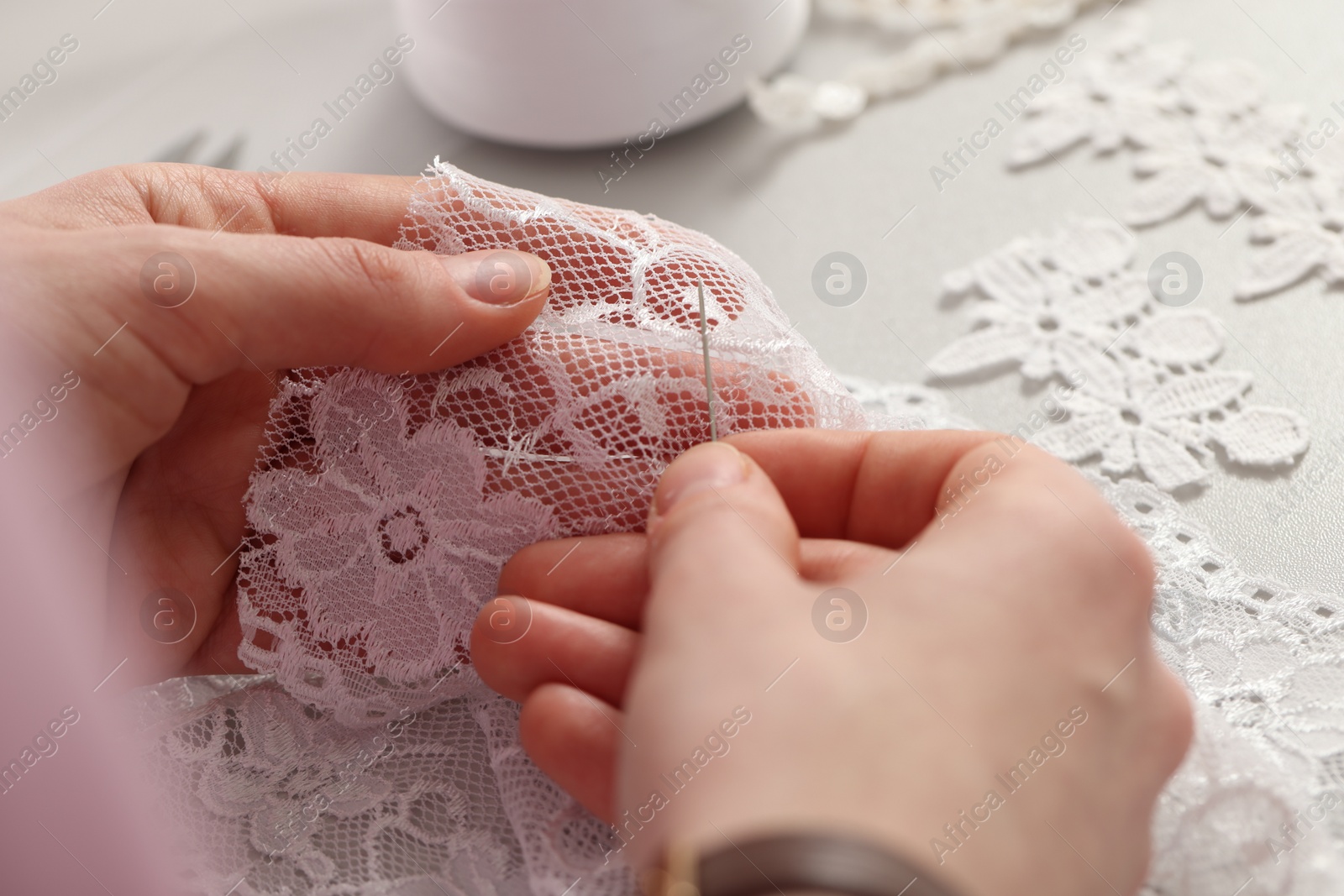 Photo of Dressmaker working with beautiful white lace at table in atelier, closeup