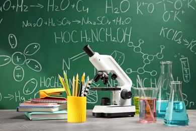 Laboratory glassware, microscope and stationery on table near chalkboard. Chemistry concept