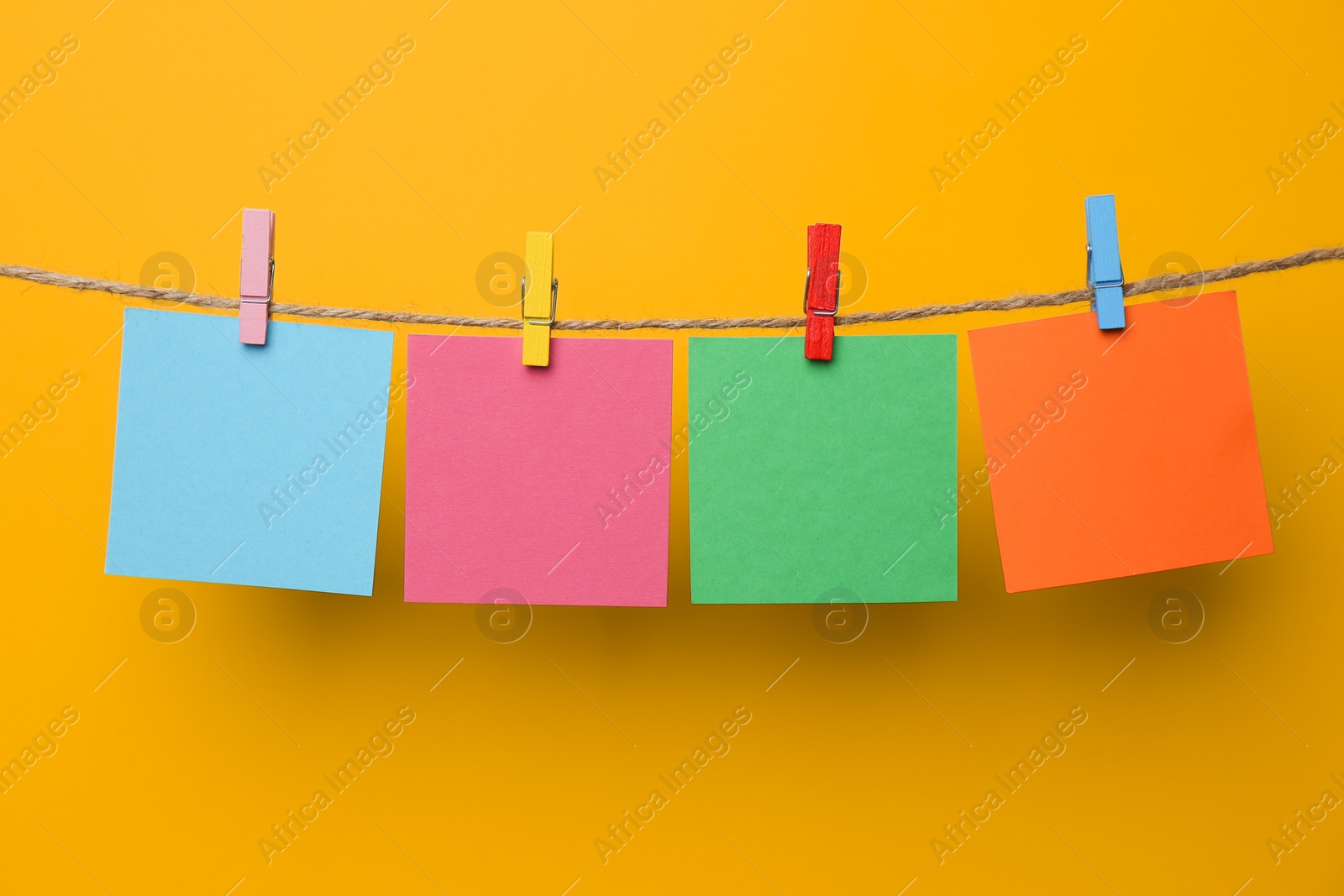 Photo of Wooden clothespins with colorful blank notepapers on twine against yellow background. Space for text