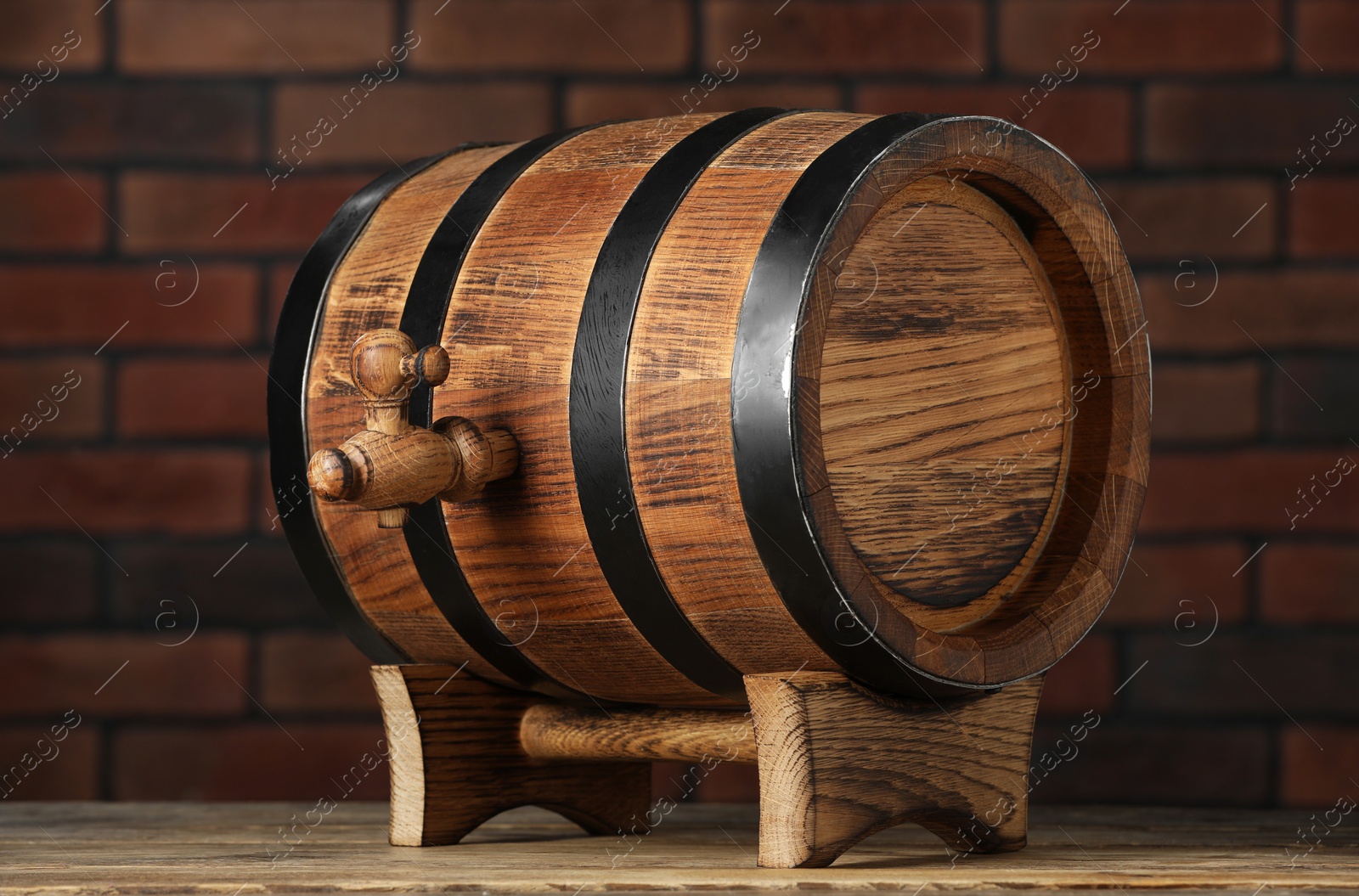 Photo of Wooden barrel with tap on table near brick wall