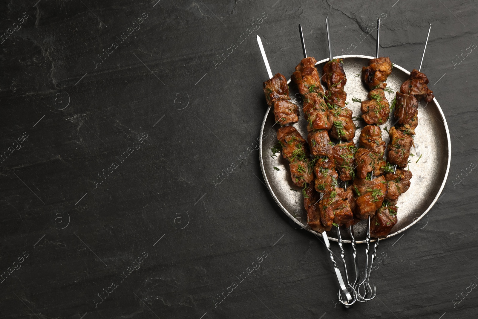 Photo of Metal skewers with delicious meat served on black table, top view. Space for text