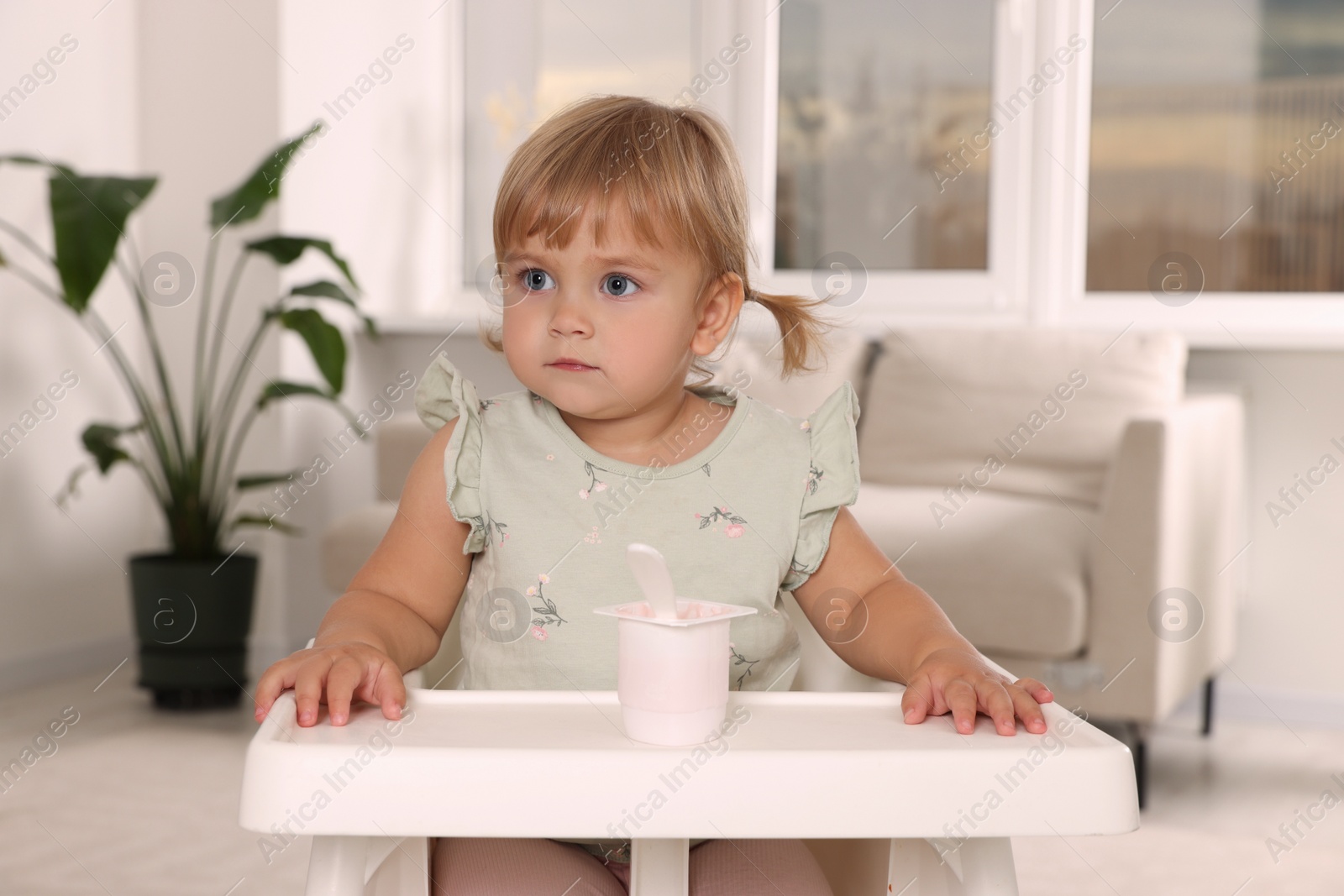 Photo of Cute little child with tasty yogurt in plastic cup at home