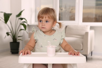 Cute little child with tasty yogurt in plastic cup at home