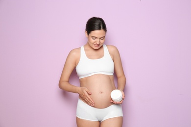 Pregnant woman holding body cream on color background