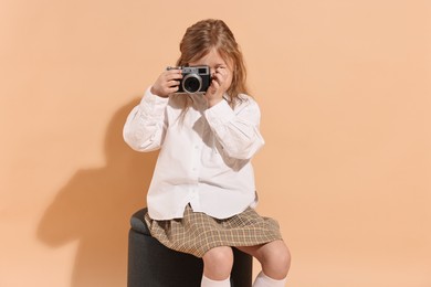 Photo of Fashion concept. Stylish girl with vintage camera on pale orange background