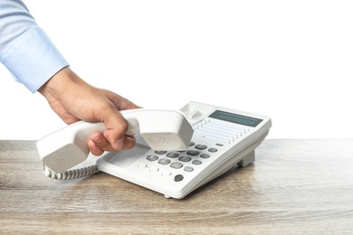 Photo of Man dialing number on telephone at table against white background, closeup