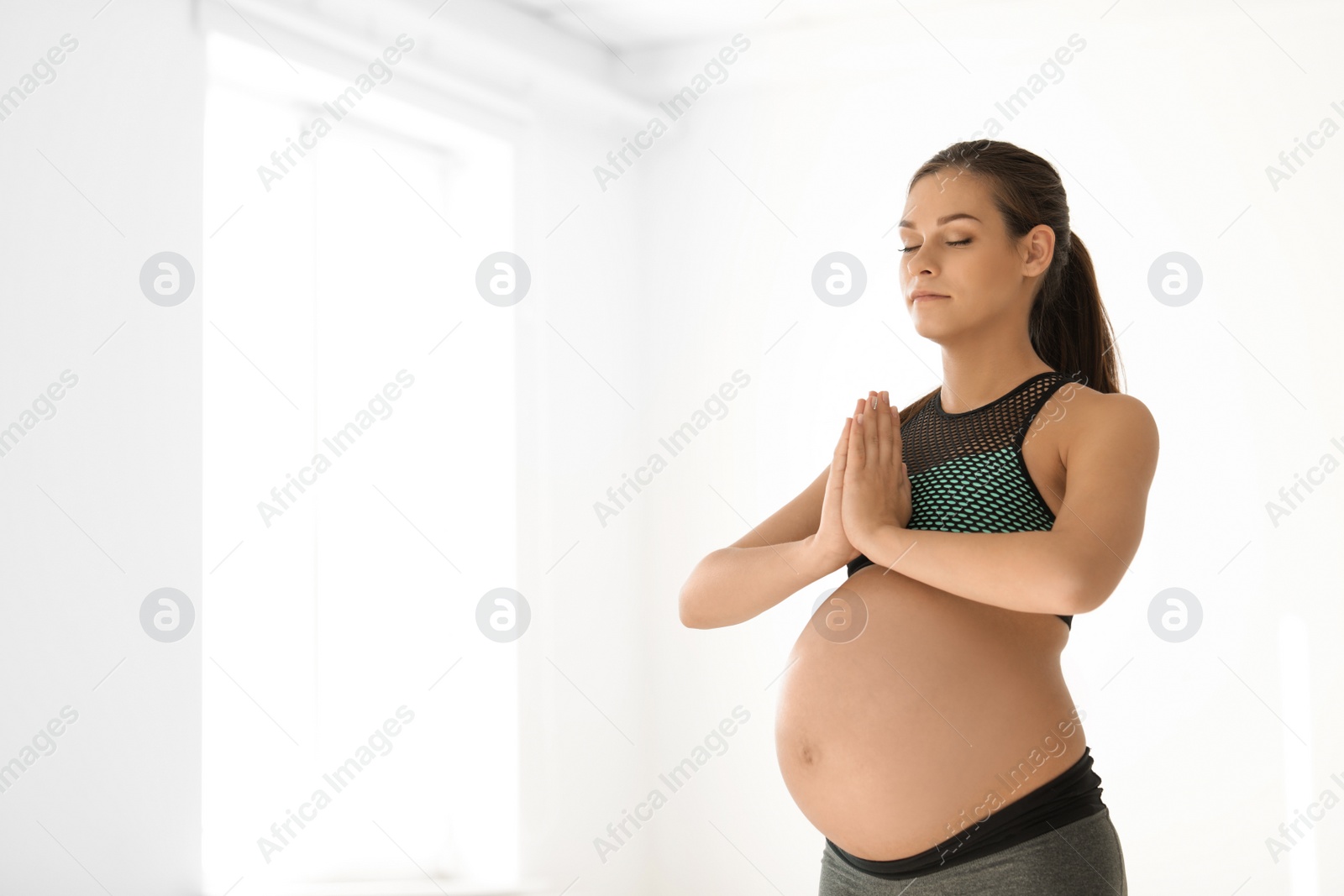 Photo of Young pregnant woman in fitness clothes practicing yoga at home. Space for text