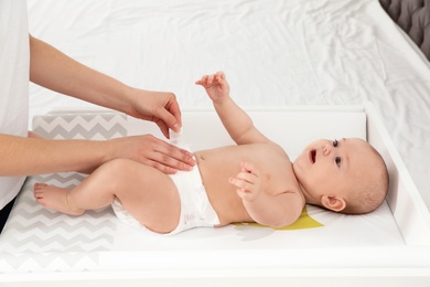 Photo of Mother changing her baby's diaper on table indoors