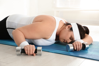 Photo of Lazy overweight woman with dumbbells sleeping on mat instead of training at gym
