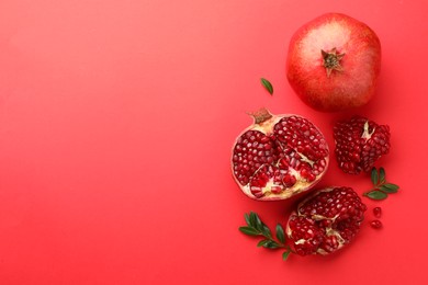 Photo of Fresh pomegranates and green leaves on red background, flat lay. Space for text