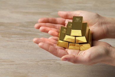 Photo of Woman holding gold bars at wooden table, closeup. Space for text