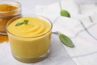 Photo of Tasty curry sauce, powder and basil leaves on white table, closeup. Space for text