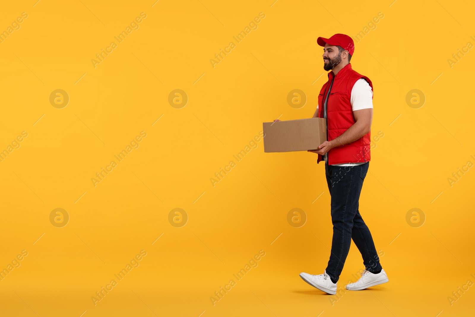 Photo of Happy young courier with parcel on orange background. Space for text