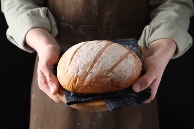 Woman holding freshly baked bread on black background, closeup