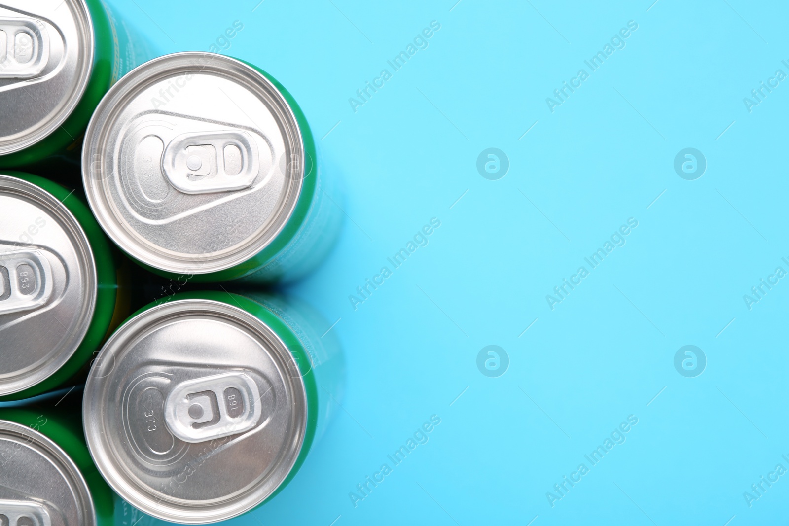 Photo of Energy drink in cans on light blue background, top view. Space for text