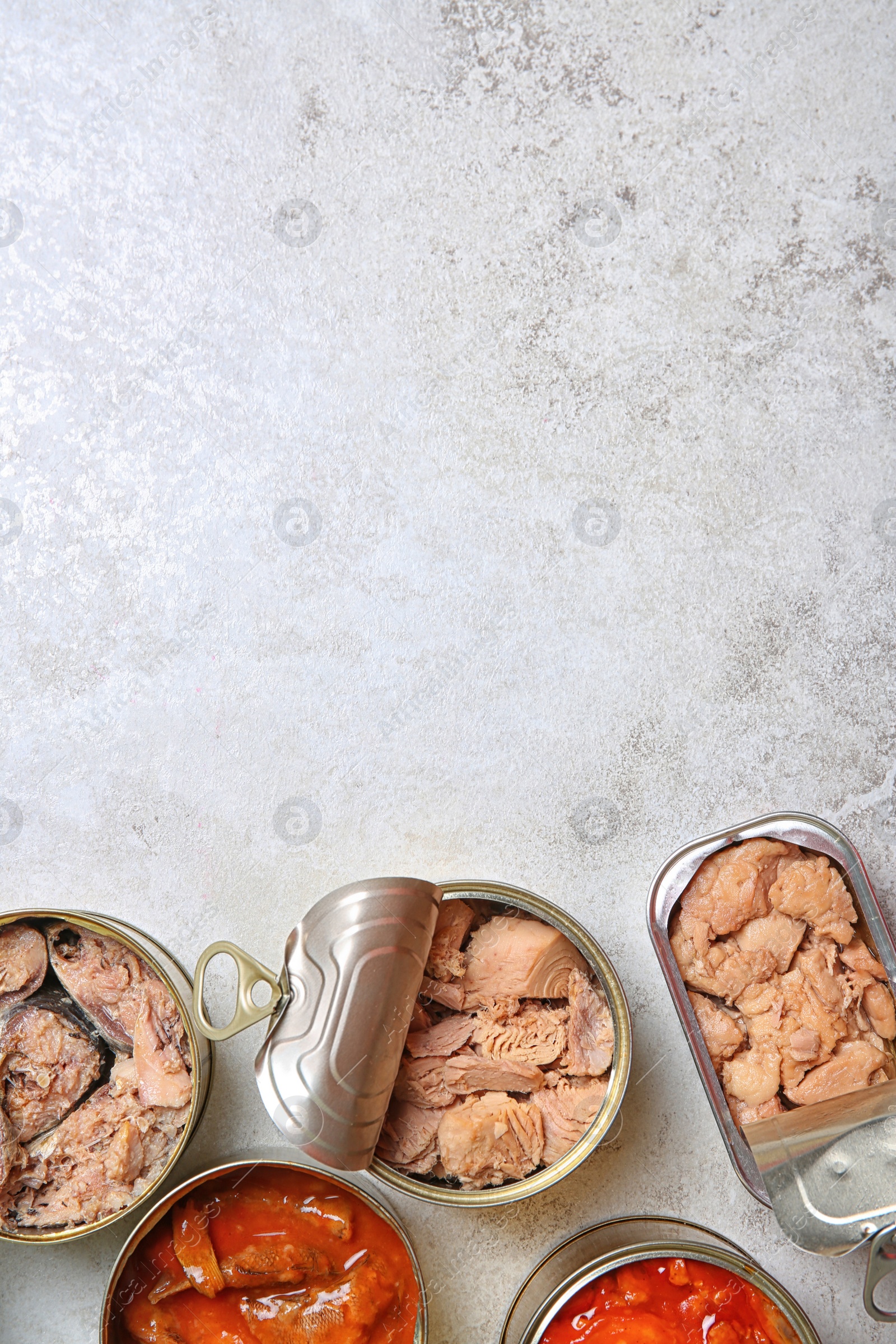 Photo of Tin cans with fish on grey table, flat lay. Space for text