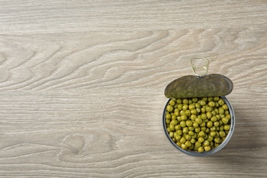 Photo of Open tin can of peas on wooden background, top view. Space for text