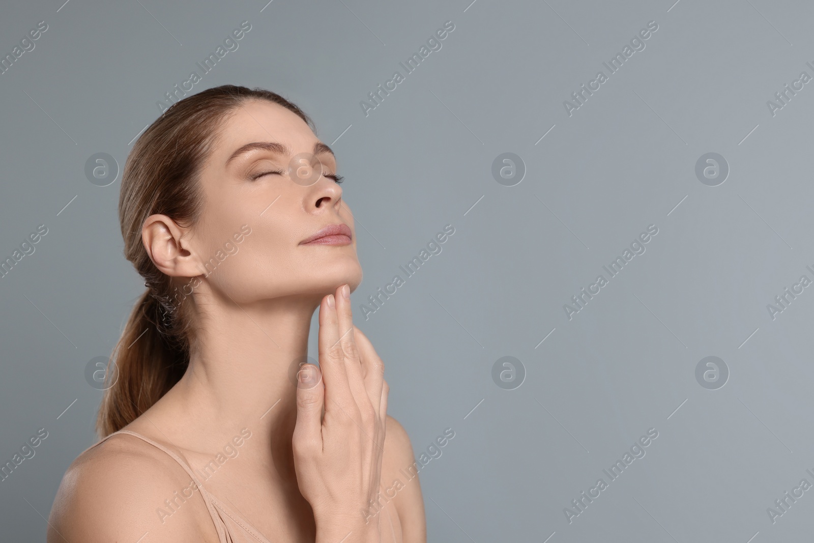 Photo of Woman massaging her face on grey background. Space for text