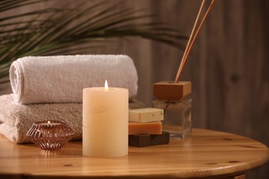 Photo of Spa composition. Burning candles, towels, soap and reed air freshener on wooden table, closeup