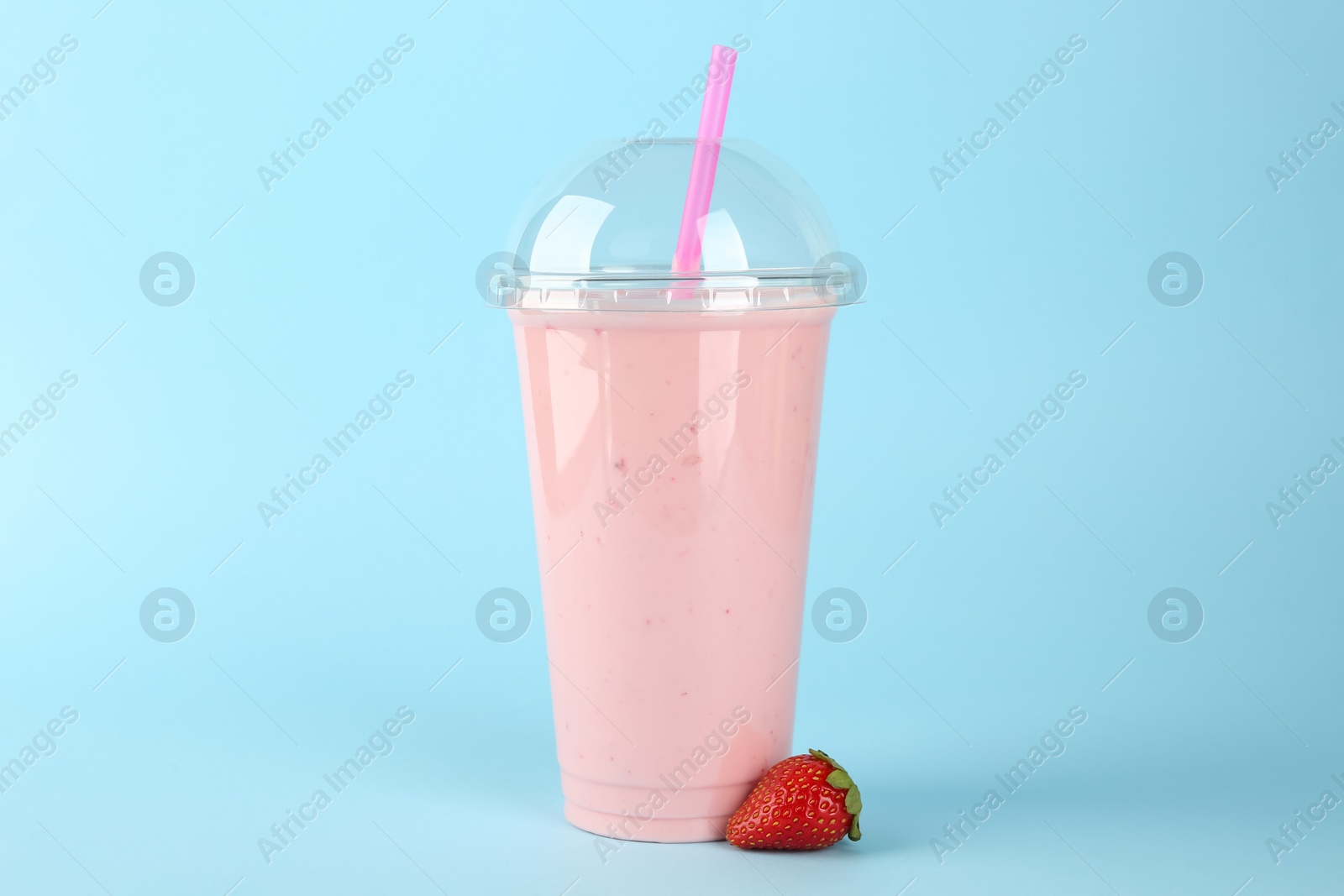 Photo of Plastic cup of tasty smoothie and fresh strawberry on light blue background