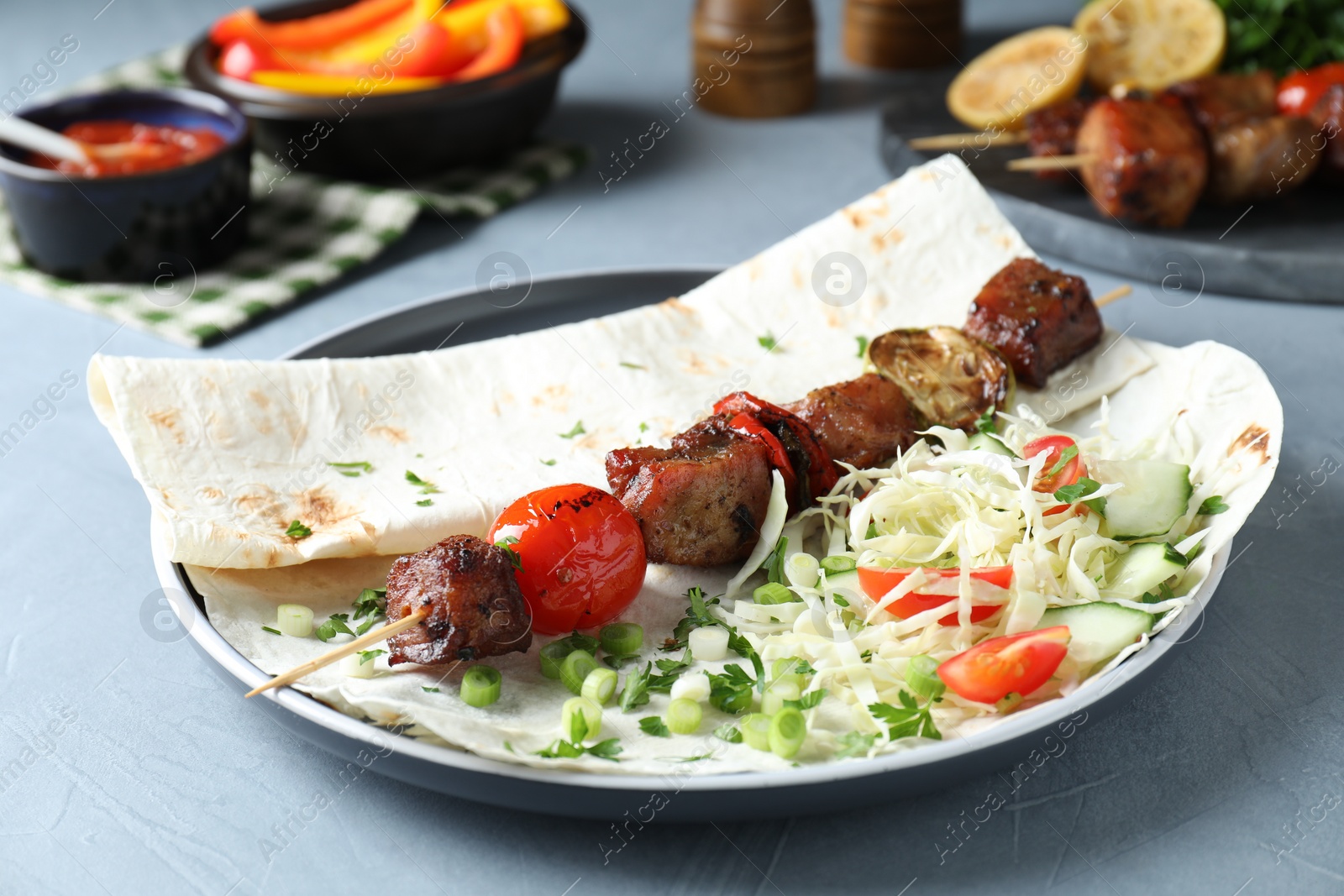 Photo of Delicious shish kebab with vegetables served on gray table, closeup