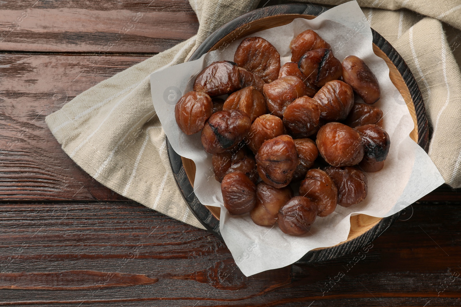 Photo of Roasted edible sweet chestnuts in bowl on wooden table, top view. Space for text