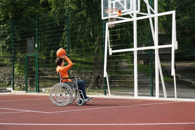 Photo of Disabled teenage boy in wheelchair playing basketball  on outdoor court