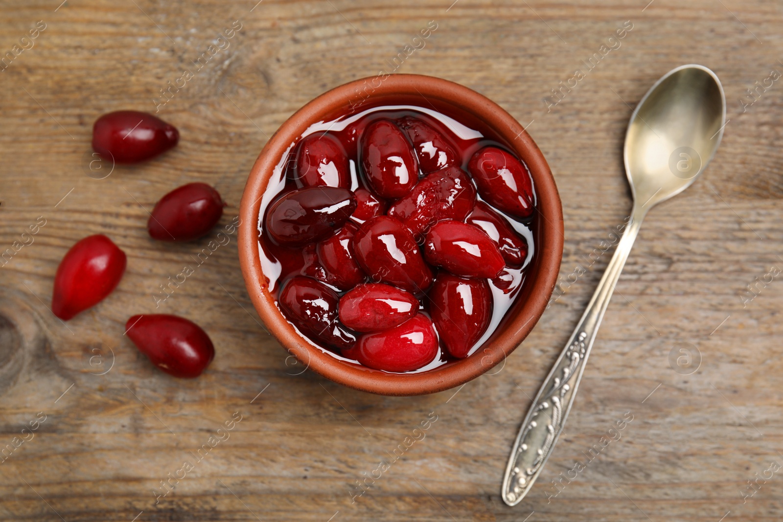 Photo of Delicious dogwood jam with berries and spoon on wooden table, flat lay