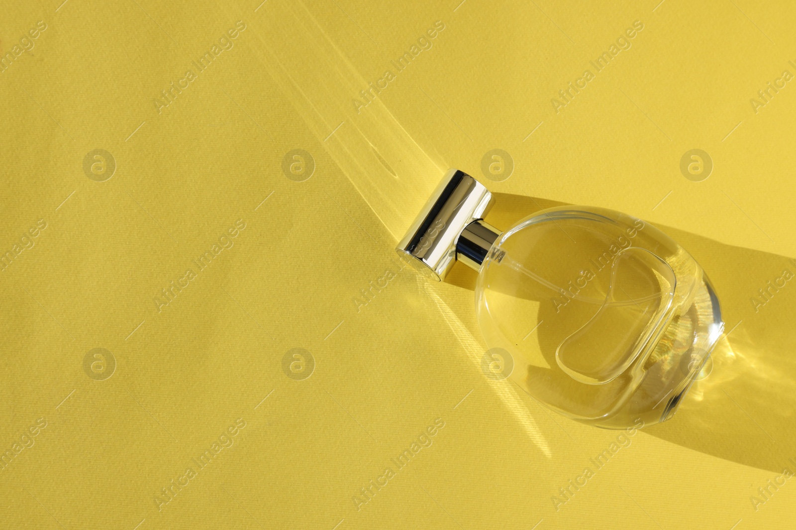 Photo of Luxury women's perfume. Sunlit glass bottle on yellow background, top view. Space for text