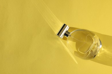 Luxury women's perfume. Sunlit glass bottle on yellow background, top view. Space for text