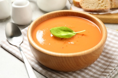Tasty creamy pumpkin soup with basil in bowl on table
