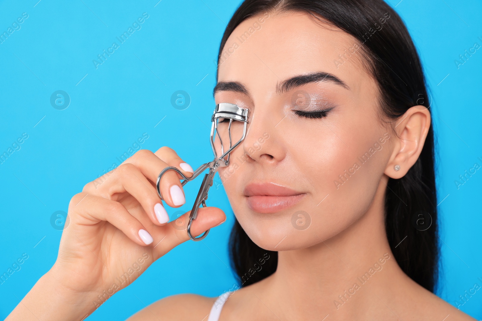 Photo of Beautiful young woman using eyelash curler on light blue background