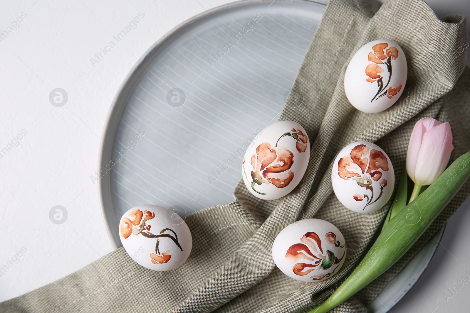 Photo of Beautifully painted Easter eggs and tulip on white table, top view