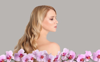 Image of Beautiful young woman and orchid flowers on light background. Spa portrait
