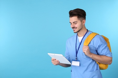 Young medical student with tablet and backpack on color background. Space for text