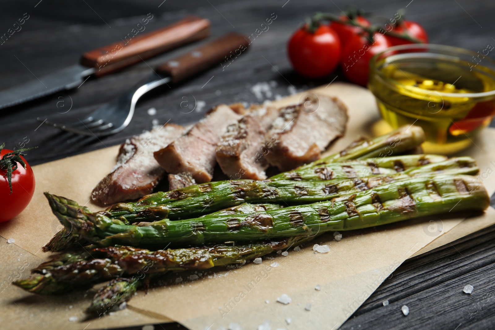 Photo of Tasty meat served with grilled asparagus on parchment, closeup